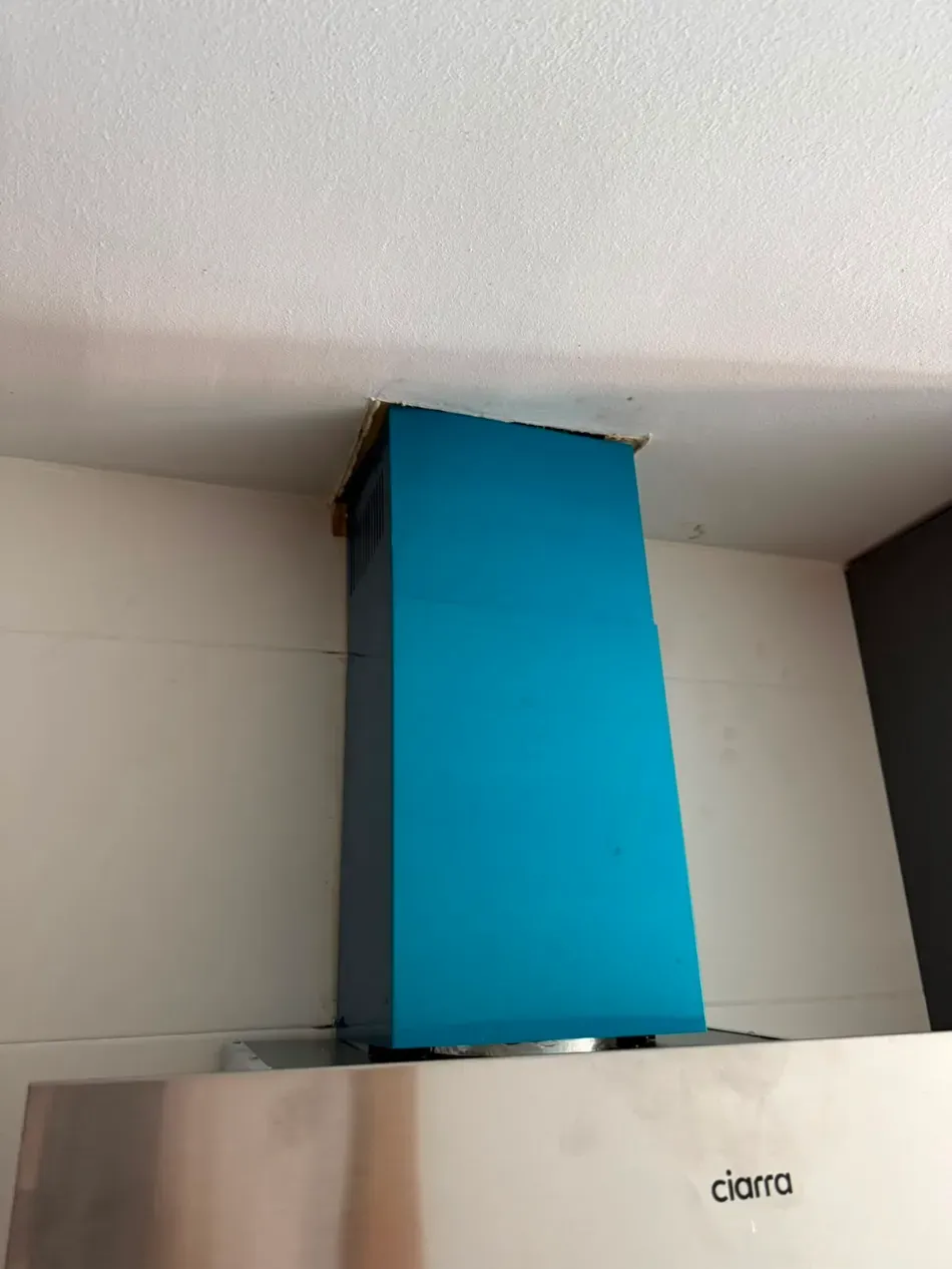 Campana extractora azul sobre una estufa de acero inoxidable debajo de un armario de pared blanco.