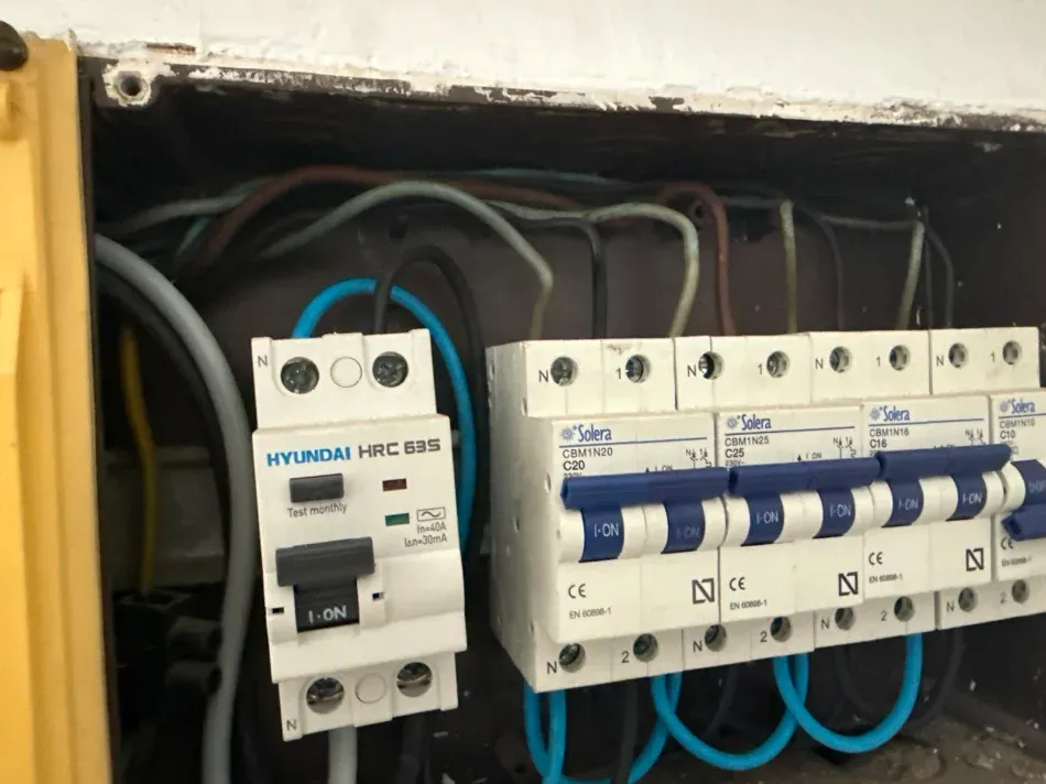 Panel de interruptores eléctricos con varios interruptores automáticos blancos y cables azules dentro de una abertura en la pared.