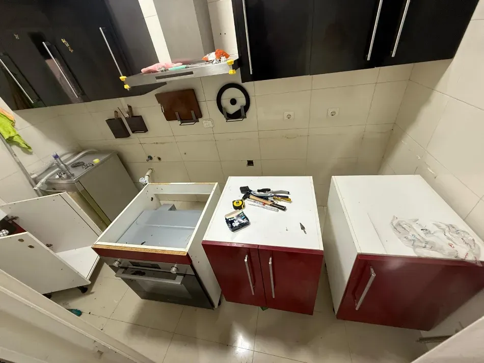 Cocina con armarios rojos y blancos, encimera blanca y utensilios esparcidos por la encimera y el suelo.