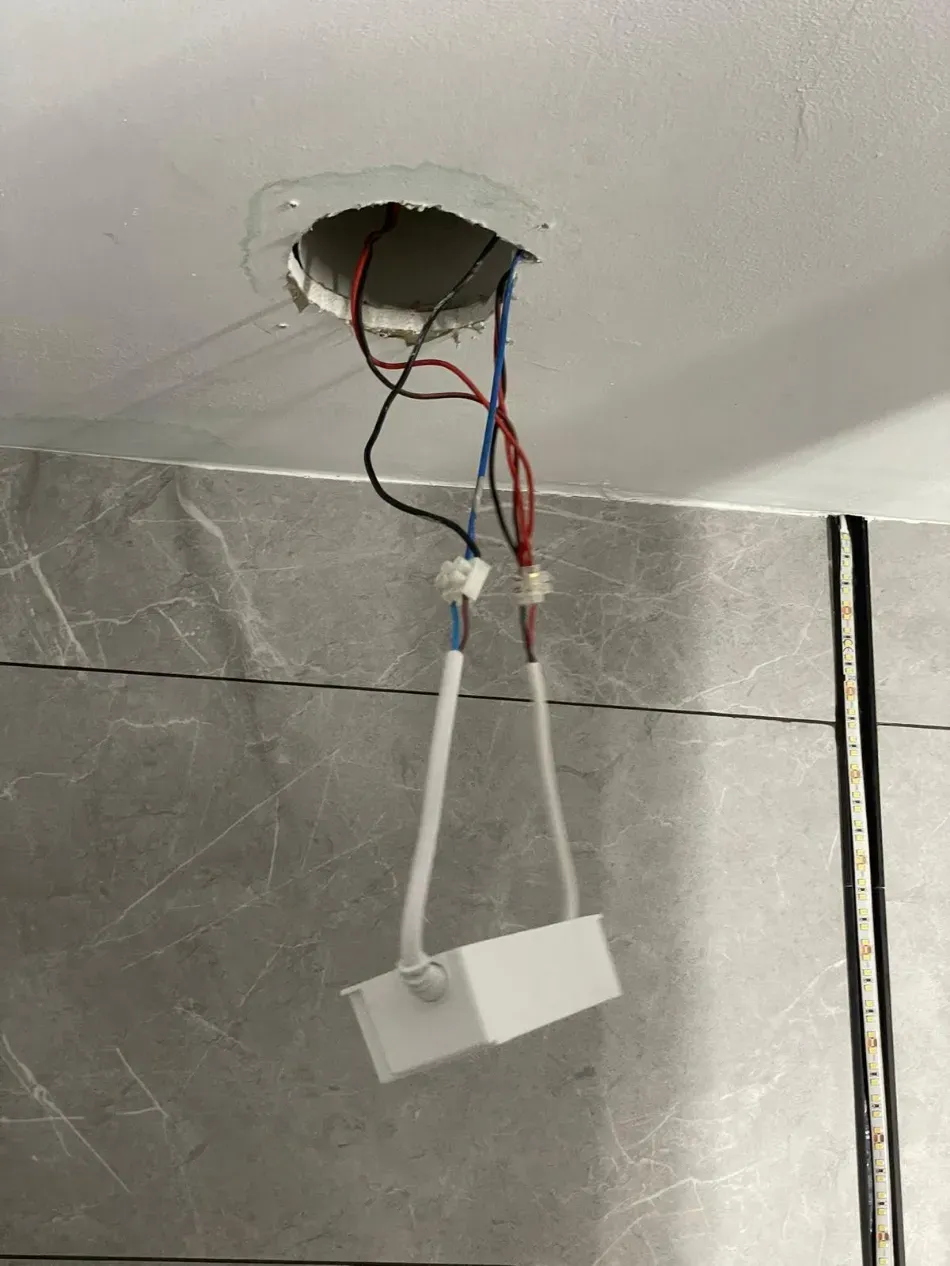Cableado del techo a la vista con una lámpara blanca colgante sobre una pared alicatada en un baño.