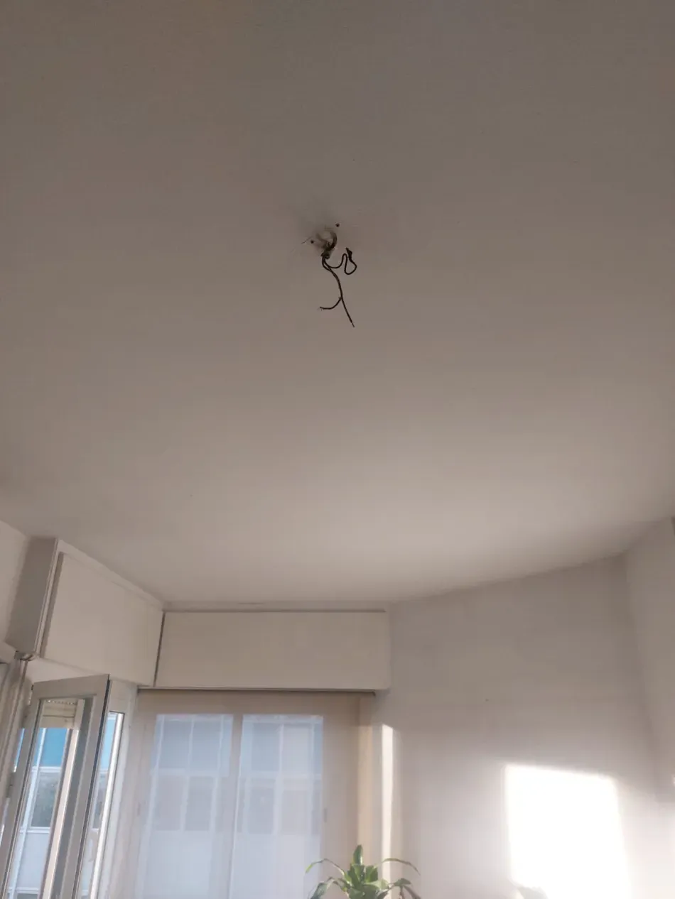 Techo blanco de la habitación con cables de lámparas colgantes a la vista sobre una ventana y luz solar brillante en la pared.