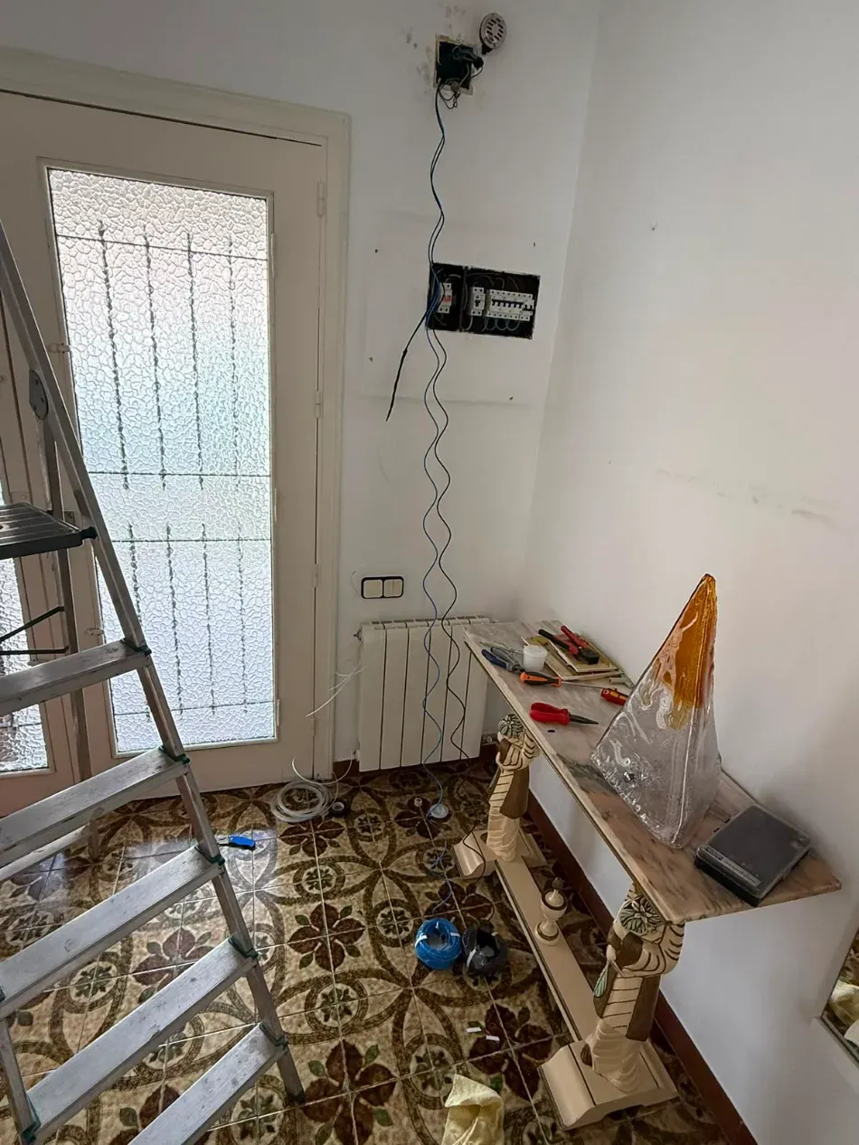 Pasillo pequeño con escalera, herramientas y un banco de trabajo cerca de una puerta y un radiador, en obras.