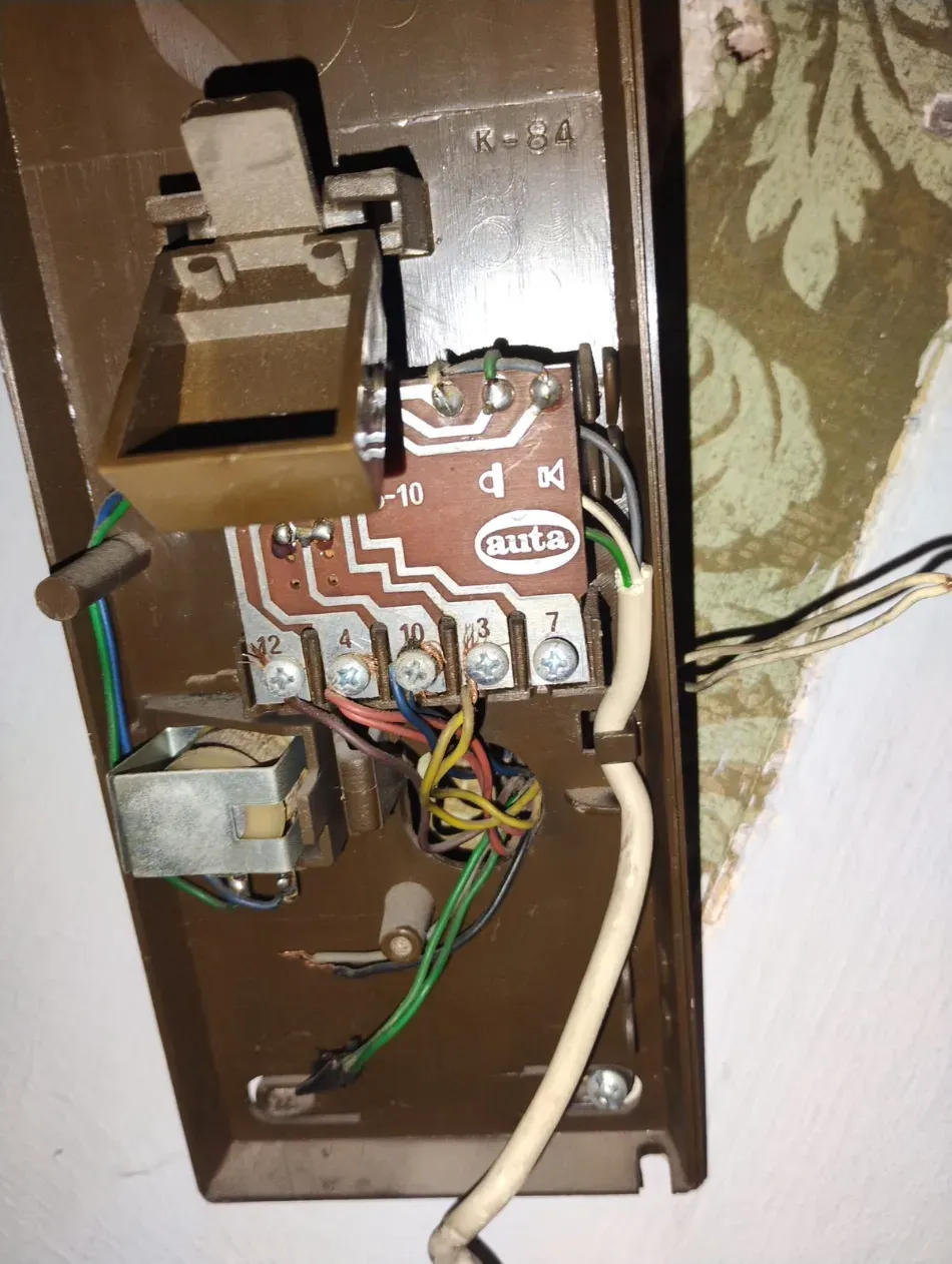 Caja de interruptor eléctrico de pared abierta con cableado expuesto y componentes de interruptor marrones.
