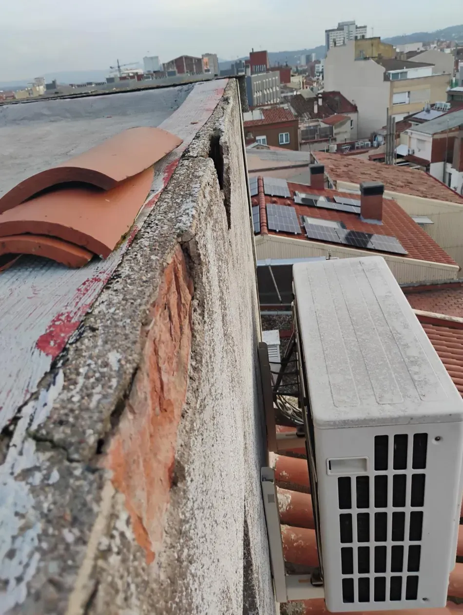 Cornisa en la azotea con vistas a los edificios, con tejas rojas y una unidad de aire acondicionado blanca.