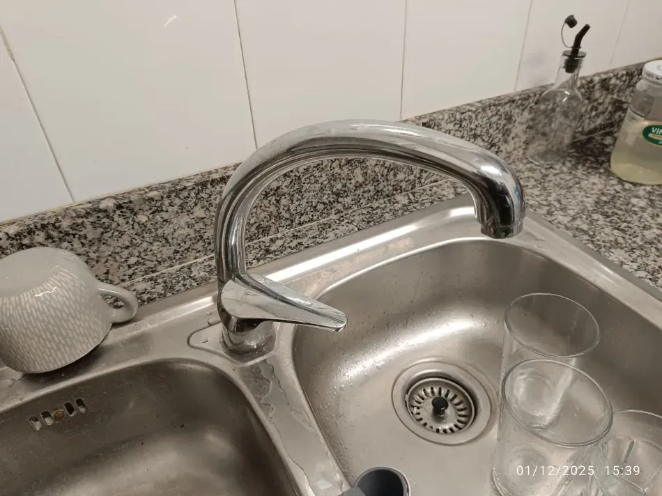 Fregadero de cocina con grifo cromado, dos vasos transparentes y un dispensador de jabón en la encimera.