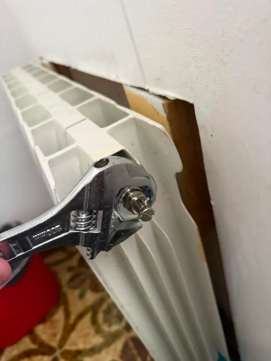 Una llave inglesa ajusta un radiador blanco montado en la pared con un panel separado de la pared.