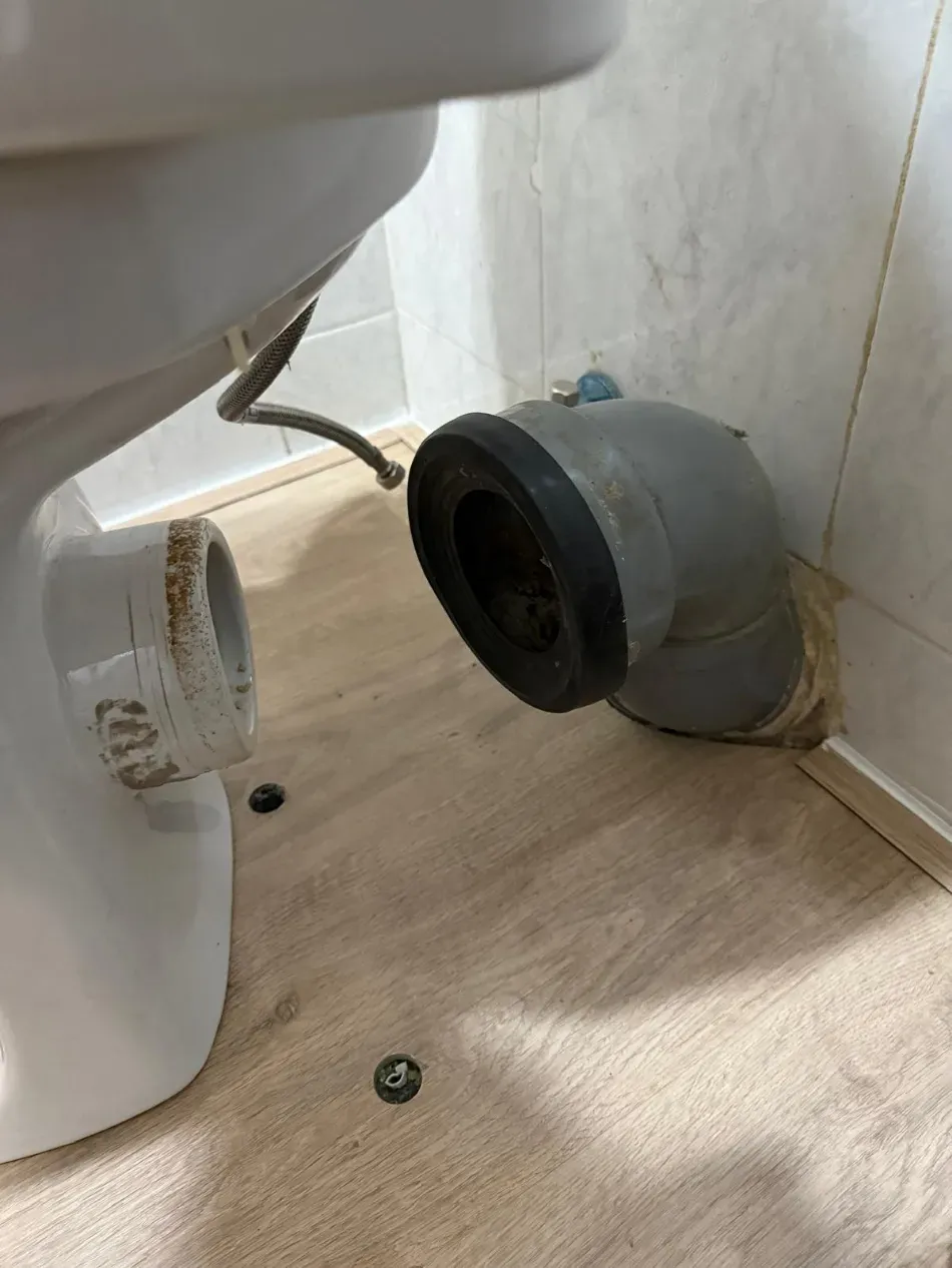 Inodoro con el tubo de desagüe gris suelto en el suelo del baño, lo que evidencia un problema de fontanería.