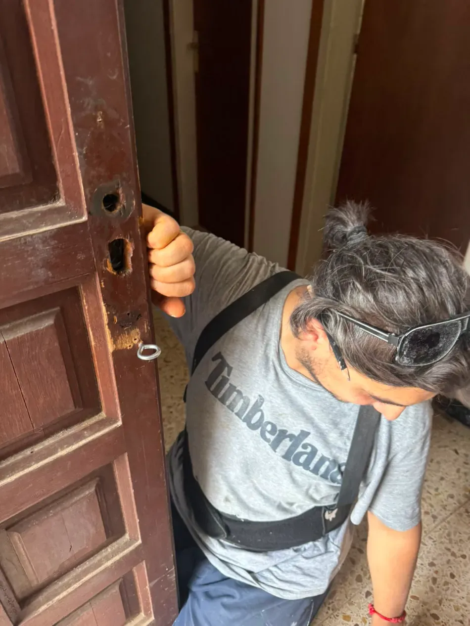 Persona que atraviesa una puerta, la mantiene abierta, vistiendo una camisa gris de Timberland y una mochila.