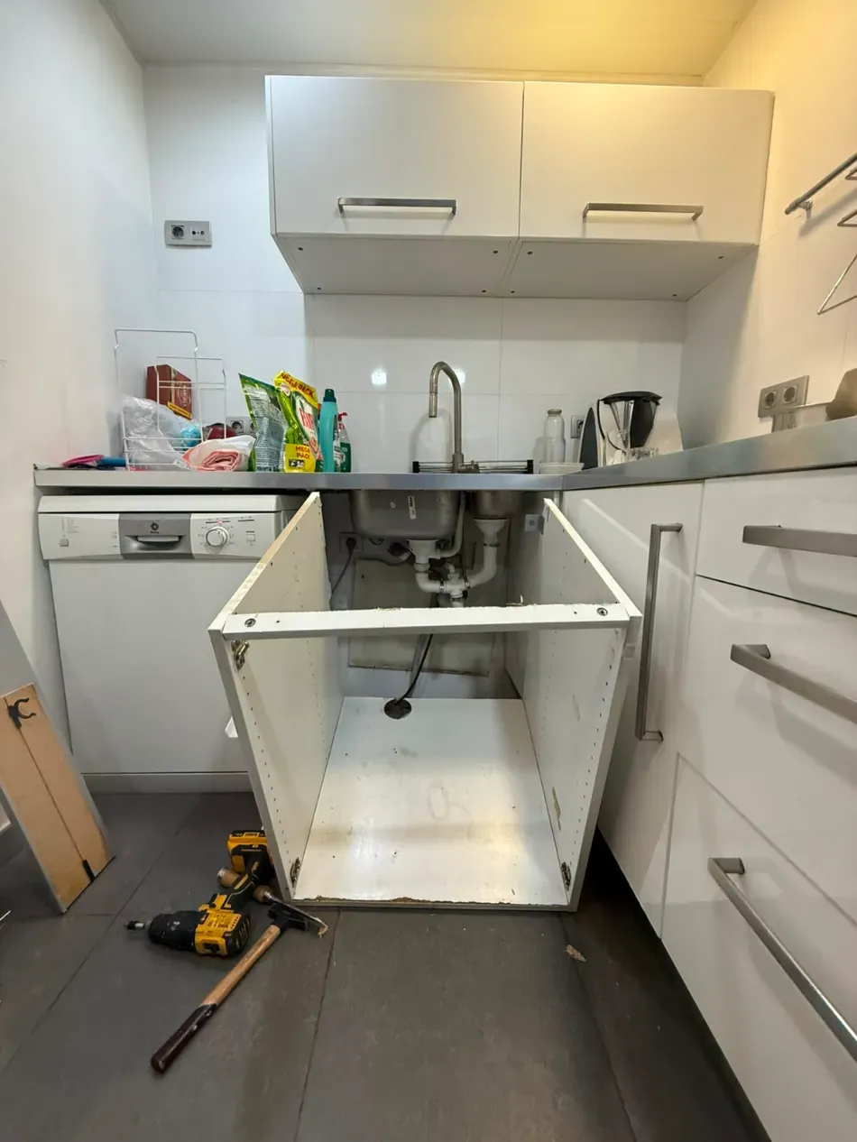 Instalación de gabinetes de cocina con fregadero abierto, utensilios en el suelo y desorden en la encimera.