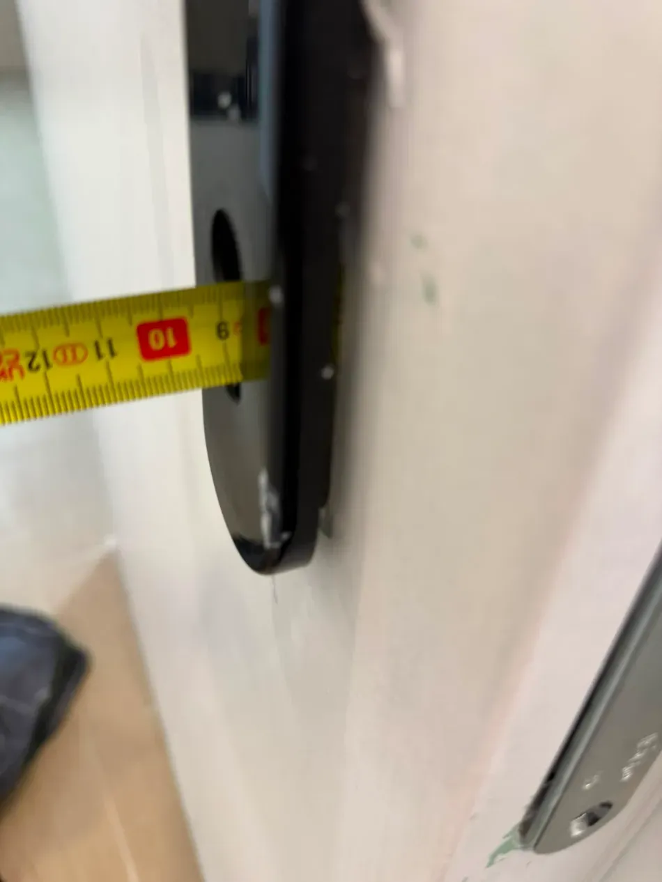 Cinta métrica para comprobar la distancia entre una pared y un objeto circular negro cerca del marco de una puerta.