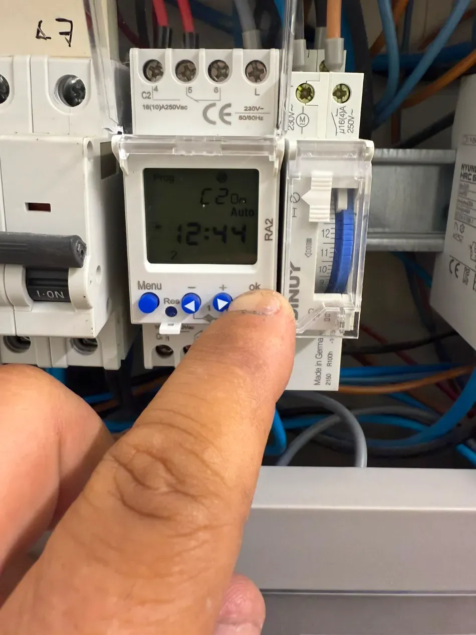 Ajustando manualmente un interruptor temporizador digital en un panel eléctrico, con botones azules y cableado visibles.