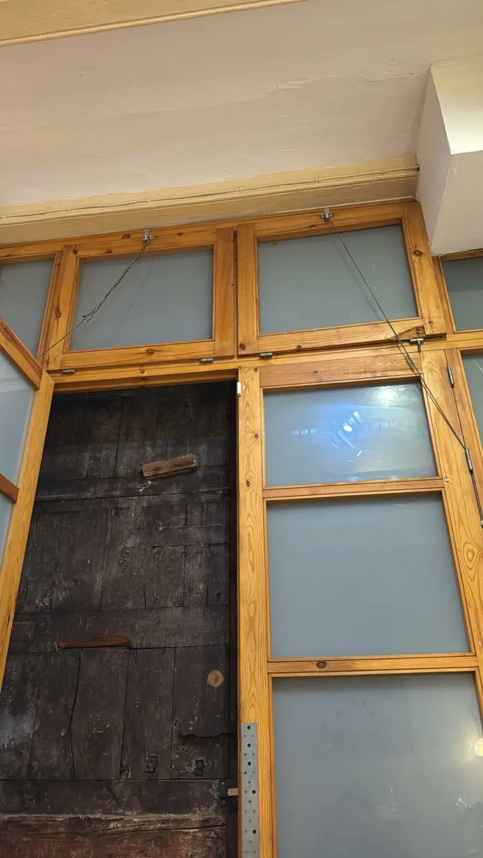 Paneles de vidrio esmerilado con marco de madera alrededor de una puerta oscura bajo un techo blanco.