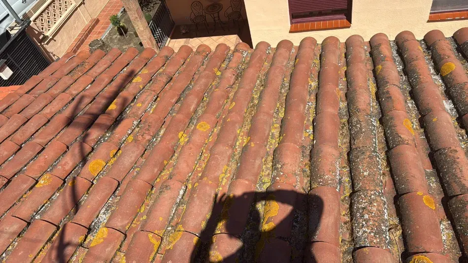 Tejado de tejas rojizas con la sombra de una persona y la sombra de una mano que sostiene una cámara.
