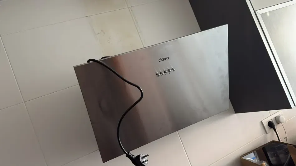 Panel metálico montado en la pared con un cable negro colgando sobre él en una habitación alicatada.