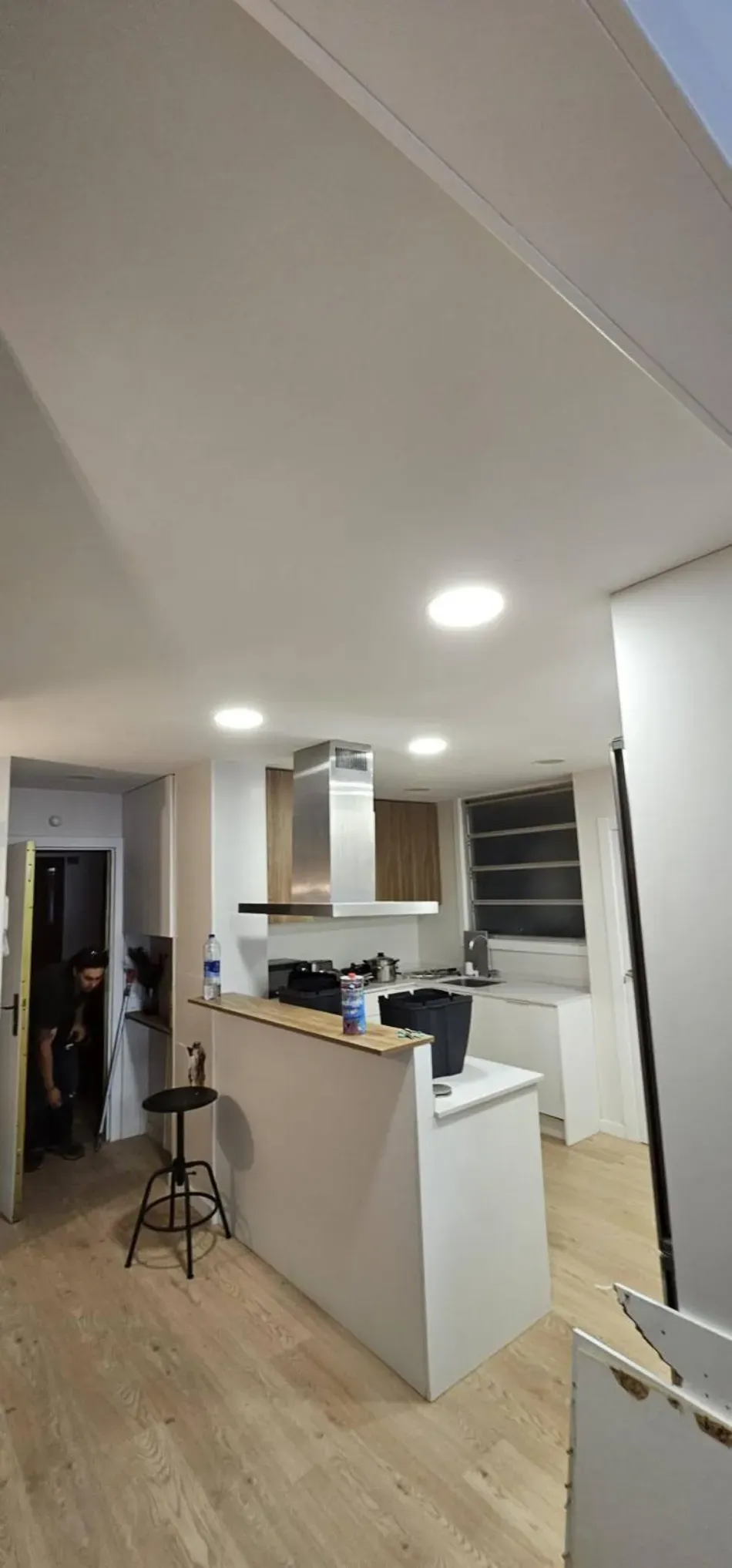 Cocina y sala de estar modernas de planta abierta con gabinetes blancos, pisos de madera y luces empotradas en el techo.