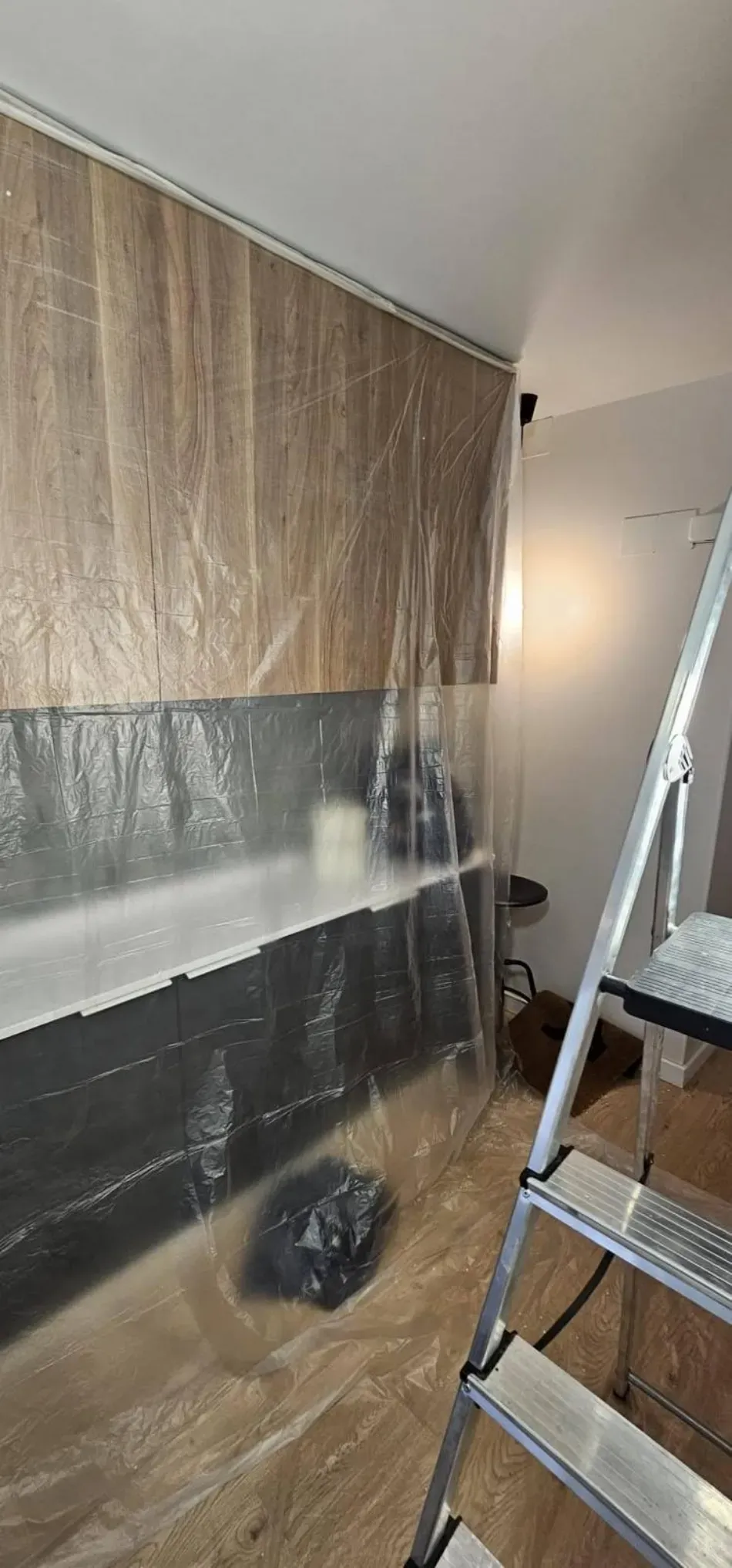Habitación en obras con paredes cubiertas de plástico, escalera y herramientas en el suelo.