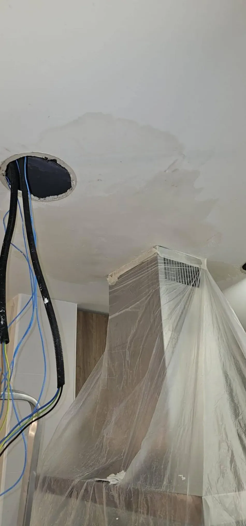 Electrodoméstico cubierto de plástico en una habitación, con cables colgando junto a un soporte de pared.
