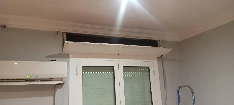 Pared interior blanca con un aire acondicionado encima de una ventana y un cable colgando a la derecha.