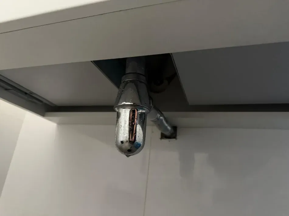 Tubería de desagüe cromada del fregadero debajo de la encimera con una fuga o daño visible.