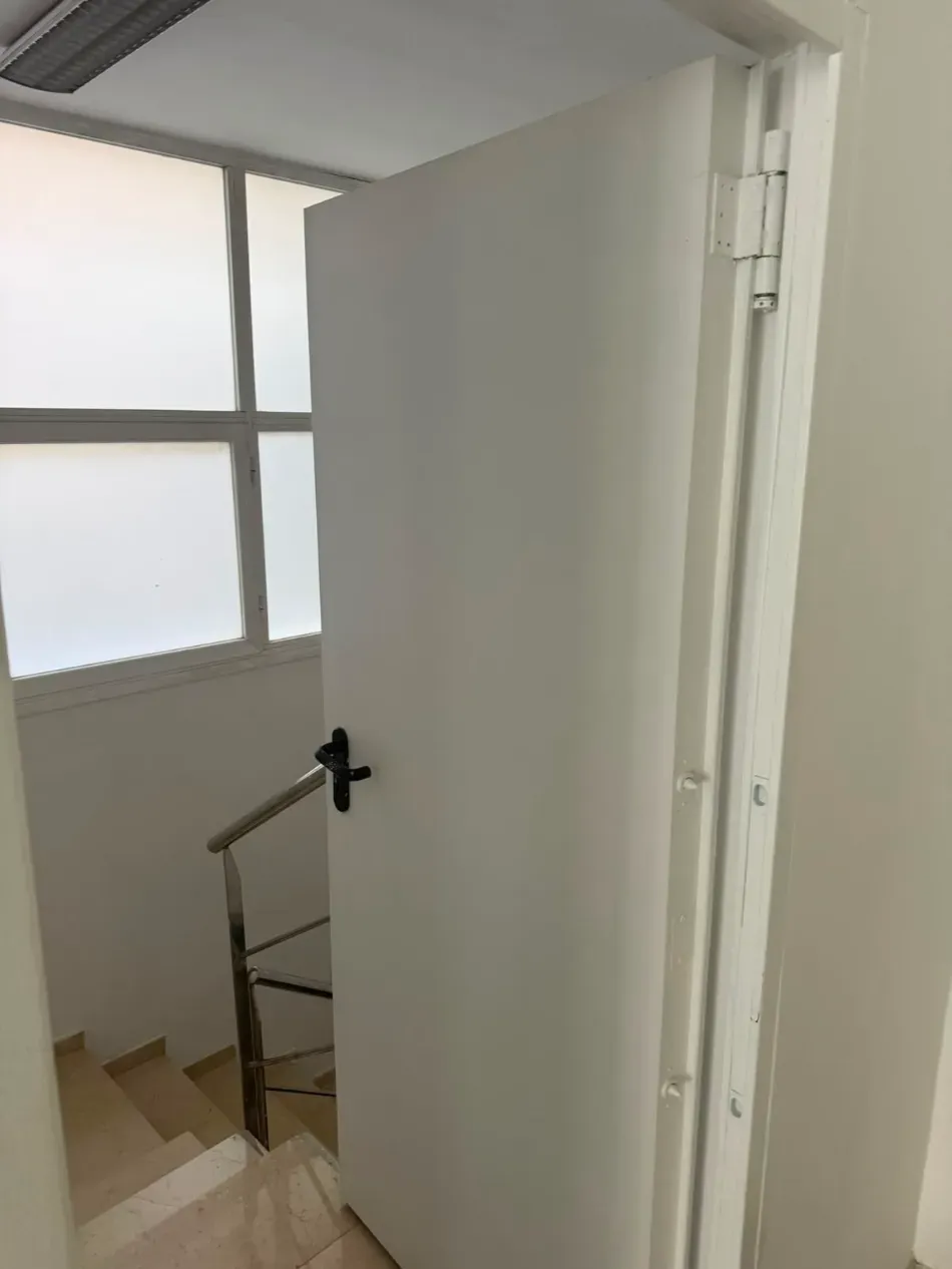 Una puerta blanca abierta se encuentra al final de una escalera, junto a una ventana esmerilada.