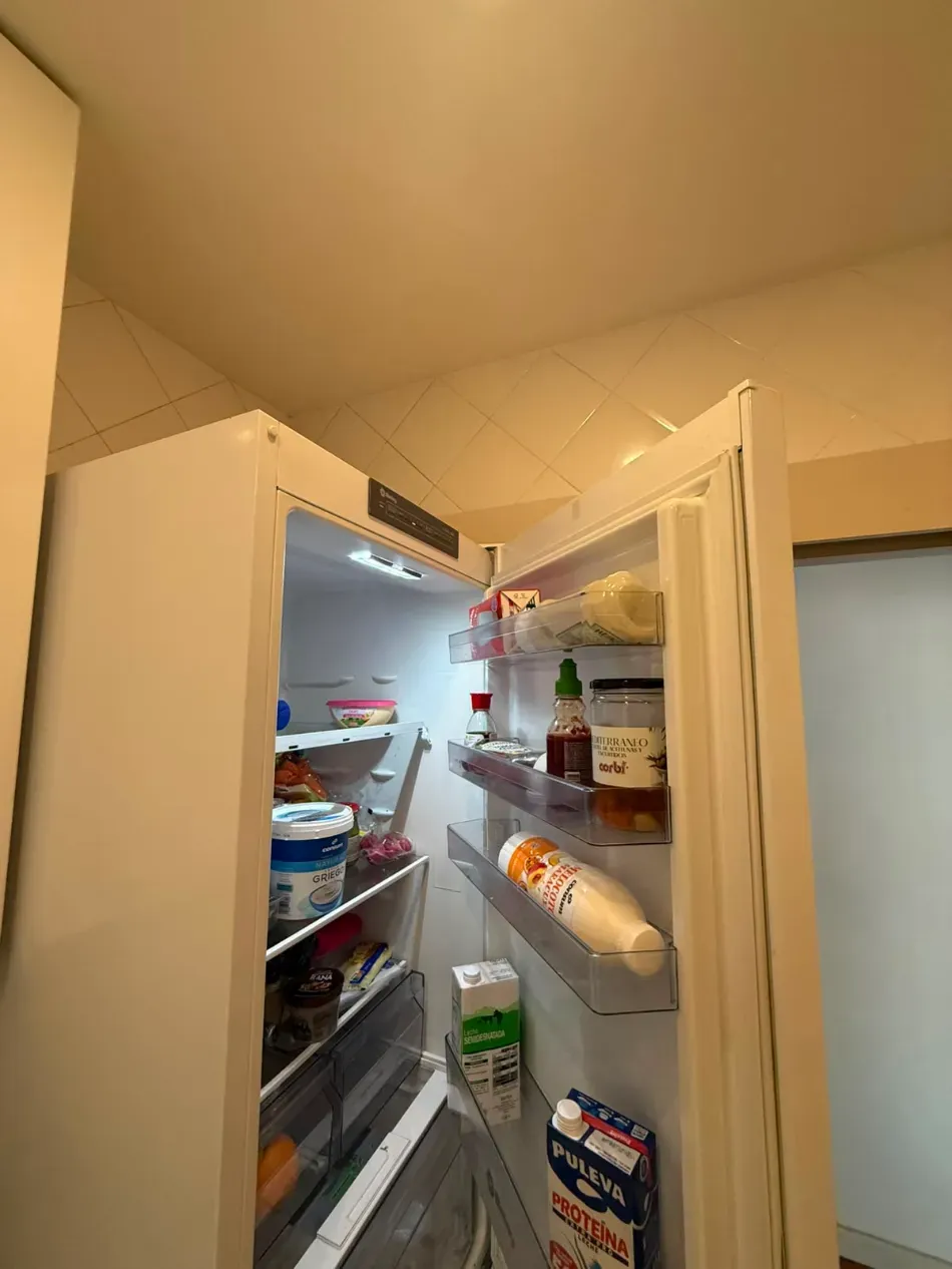 En una cocina, se puede abrir un refrigerador con estantes llenos de alimentos y bebidas.