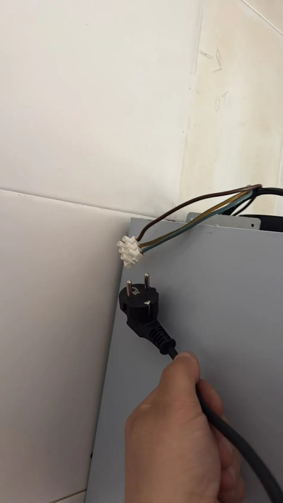 Conectando manualmente un cable negro a un aparato gris junto a una pared de azulejos.