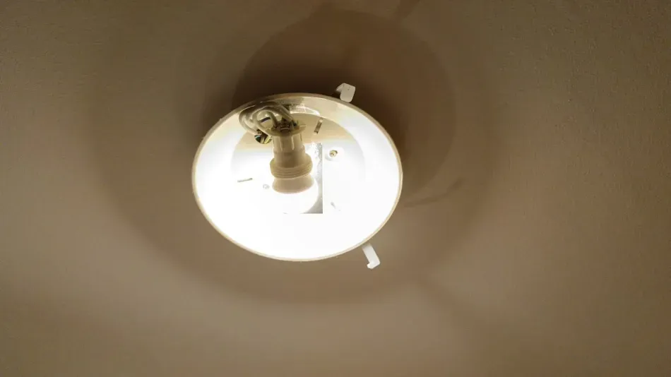 Lámpara de techo con bombilla brillante sobre un techo beige.