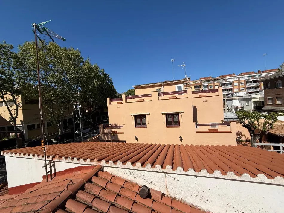 Vista desde la azotea de tejados de terracota y edificios de color beige bajo un cielo azul despejado, con árboles y antenas.