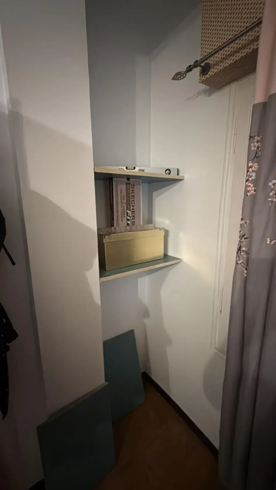 Pequeño rincón vacío de armario con estantes, una barra para colgar ropa y un cubo de basura beige.