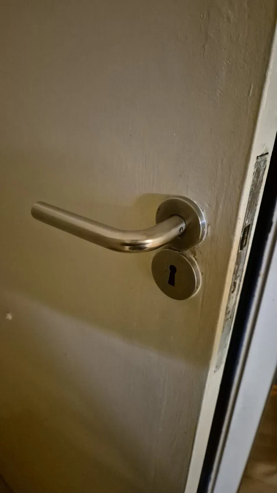 Primer plano de una puerta beige con manilla y cerradura plateadas.