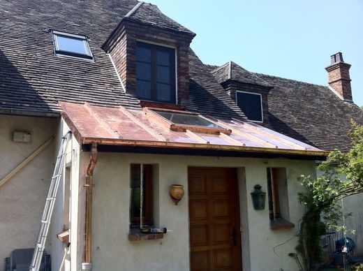 Entrée d'une petite maison avec un toit délabré, une porte en bois et des lucarnes sous un toit de tuiles.