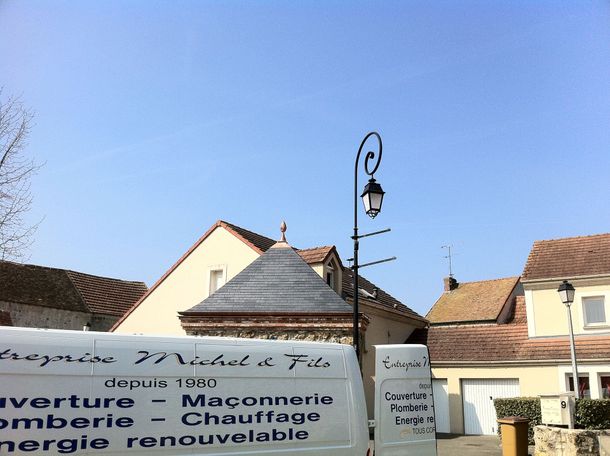 Camionnette et toiture d'un bâtiment sur une place ensoleillée, avec un lampadaire et un ciel bleu.