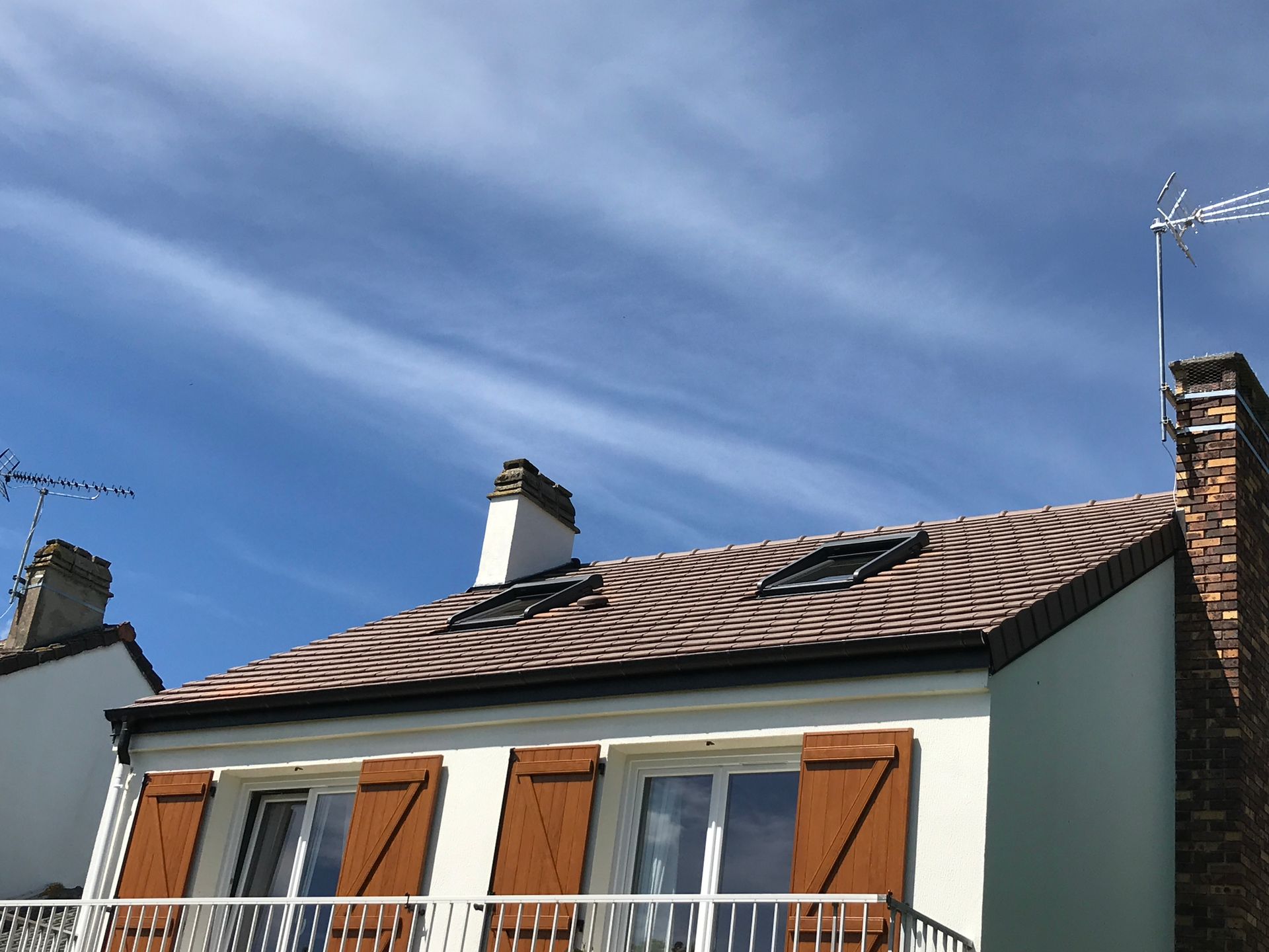 Maison aux volets bruns et au toit de tuiles sous un ciel bleu.