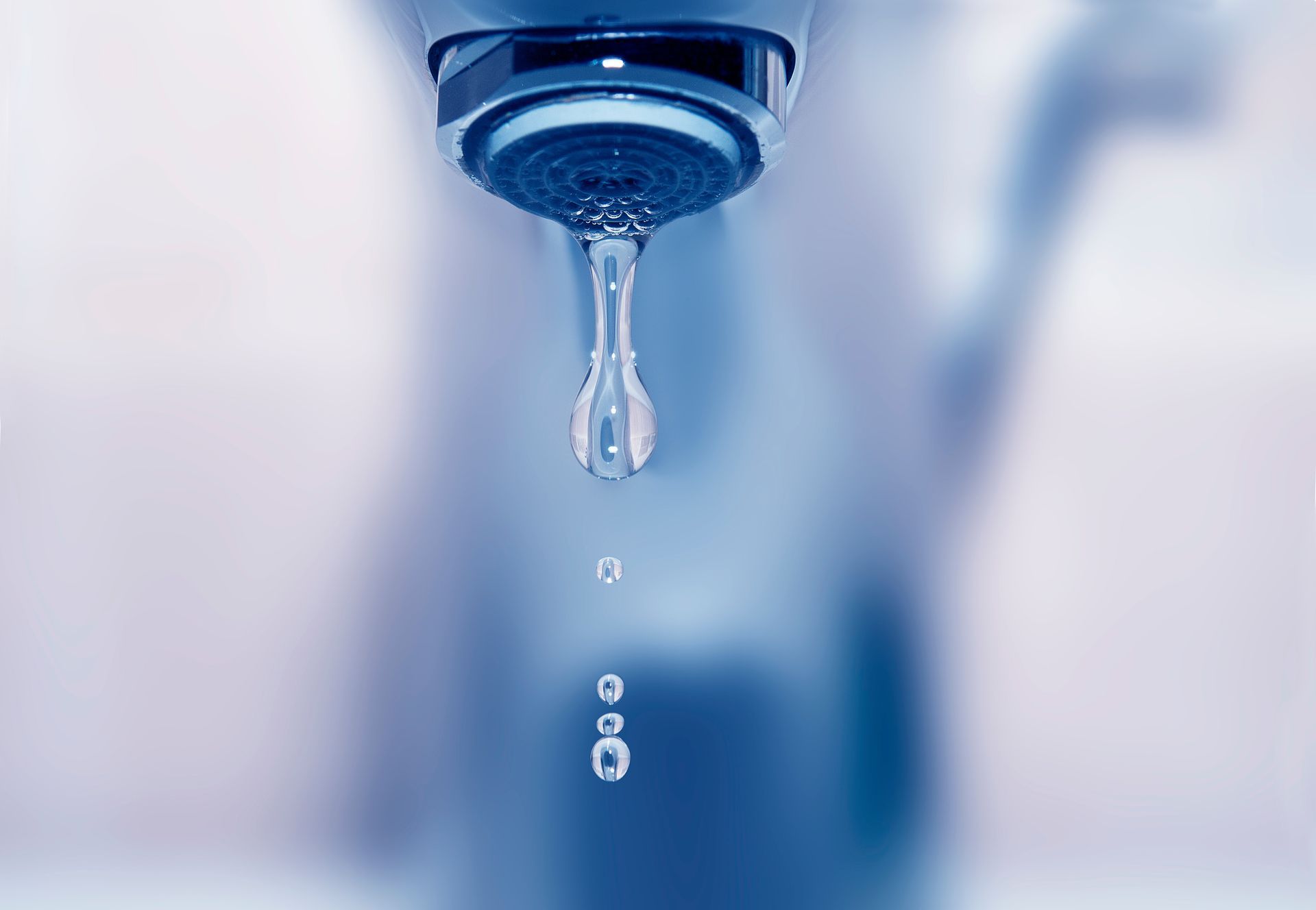 Gros plan sur un robinet chromé laissant couler de l'eau dans un évier dont la surface est floue.