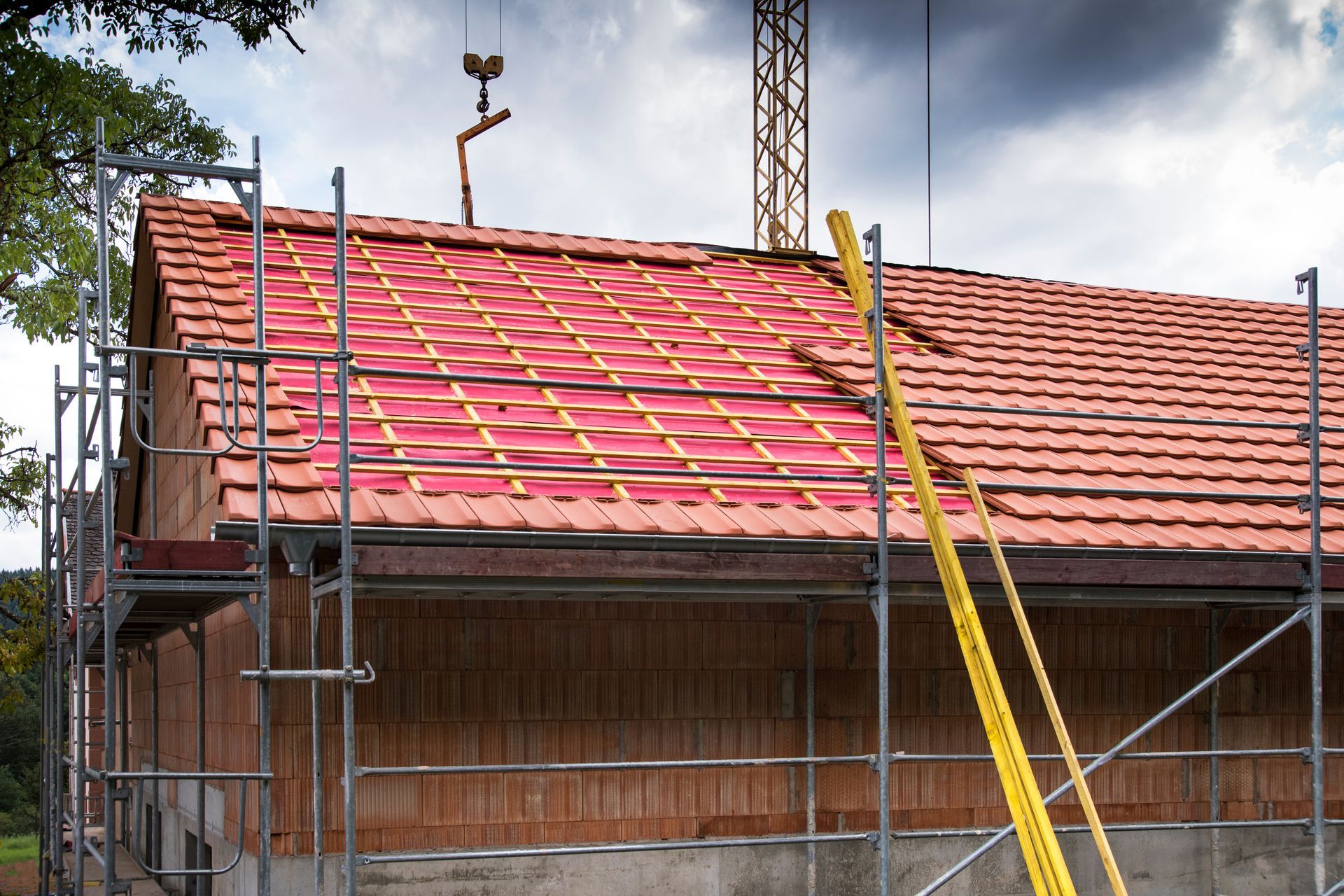 Toiture en construction avec tuiles rouges, échafaudages et poutres de soutien jaunes sous un ciel nuageux.