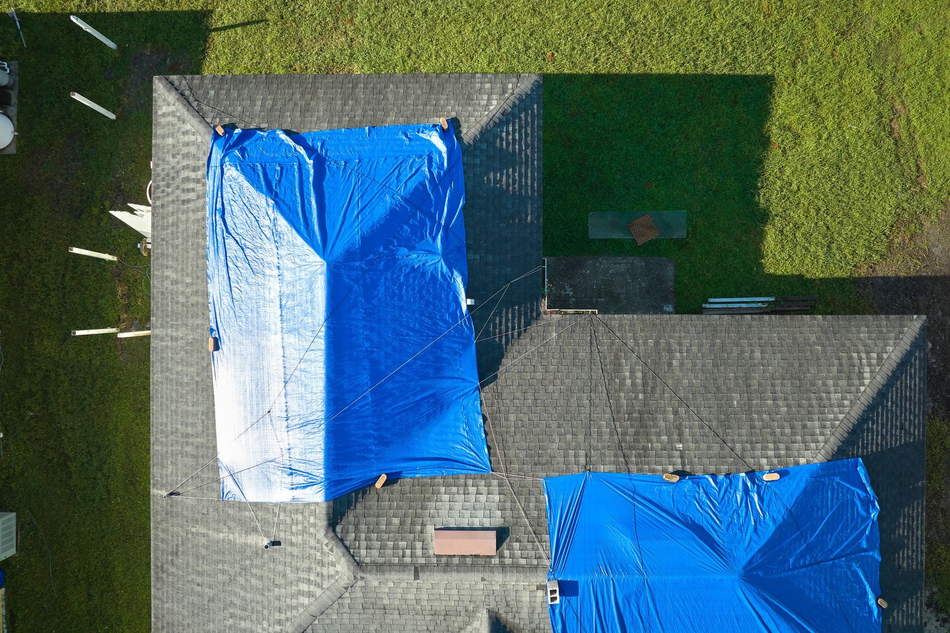 Vue aérienne d'un toit de maison recouvert de bâches bleues et d'une pelouse verte environnante.