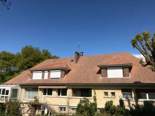 Maison de banlieue avec un toit de tuiles rouges et des lucarnes sous un ciel bleu clair.