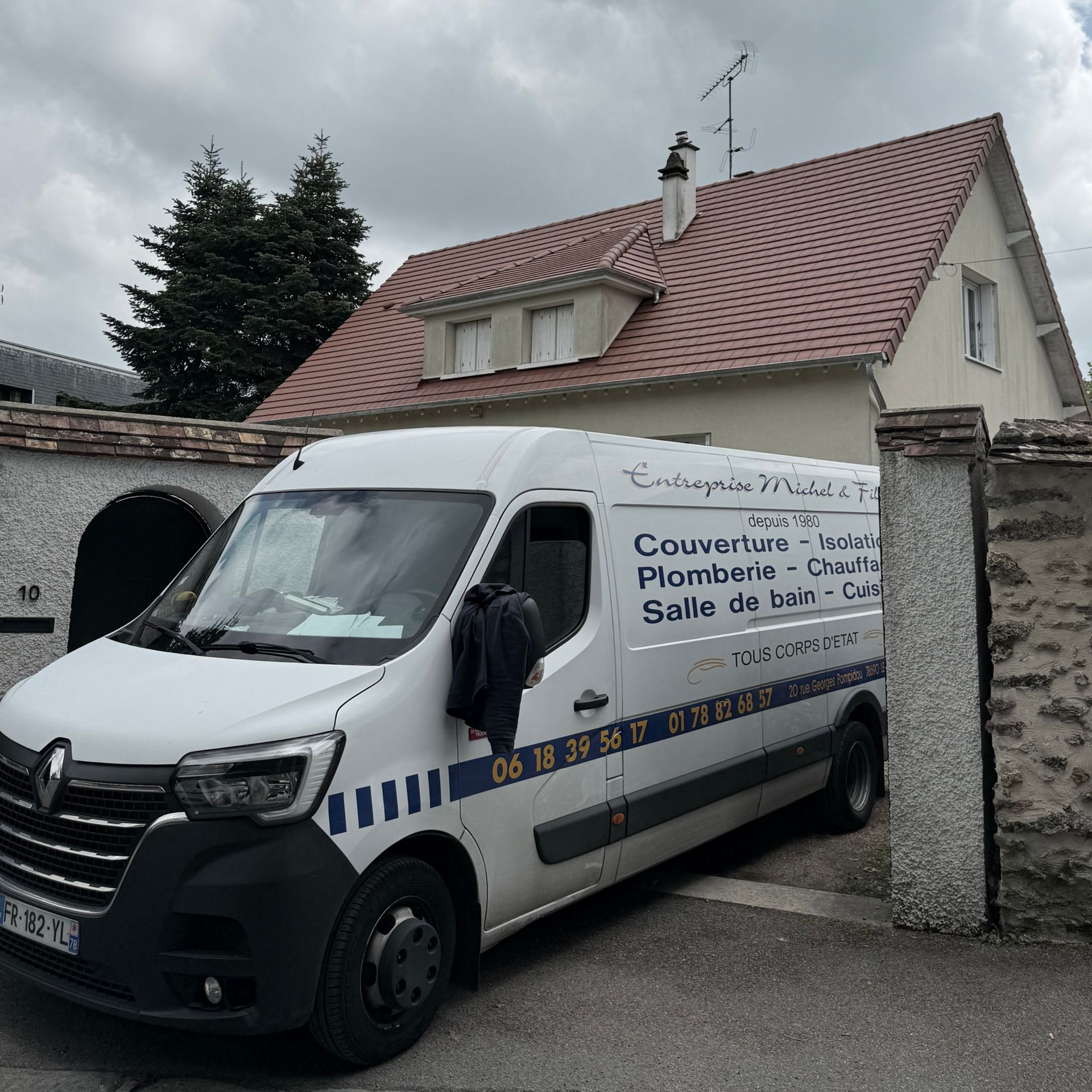 Une camionnette blanche est garée contre un muret en pierre dans une allée résidentielle.