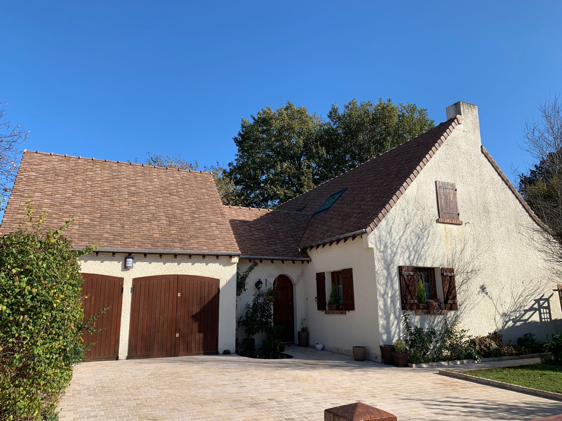 Maisonnette blanche avec double porte de garage marron et toit de tuiles sous un ciel bleu clair.