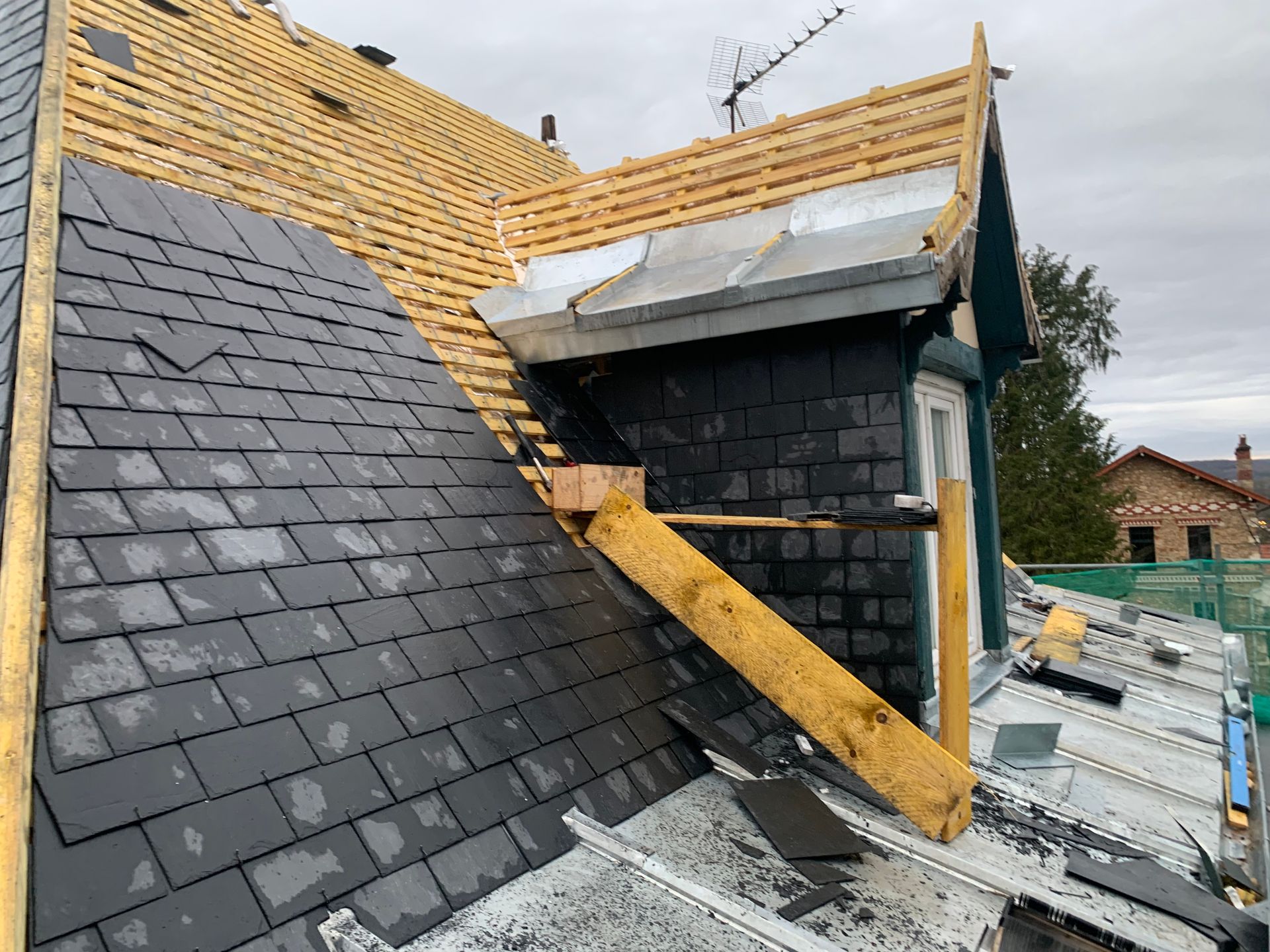Réparation de toiture avec bardeaux noirs, sous-couche apparente et supports en bois sur une lucarne de maison.