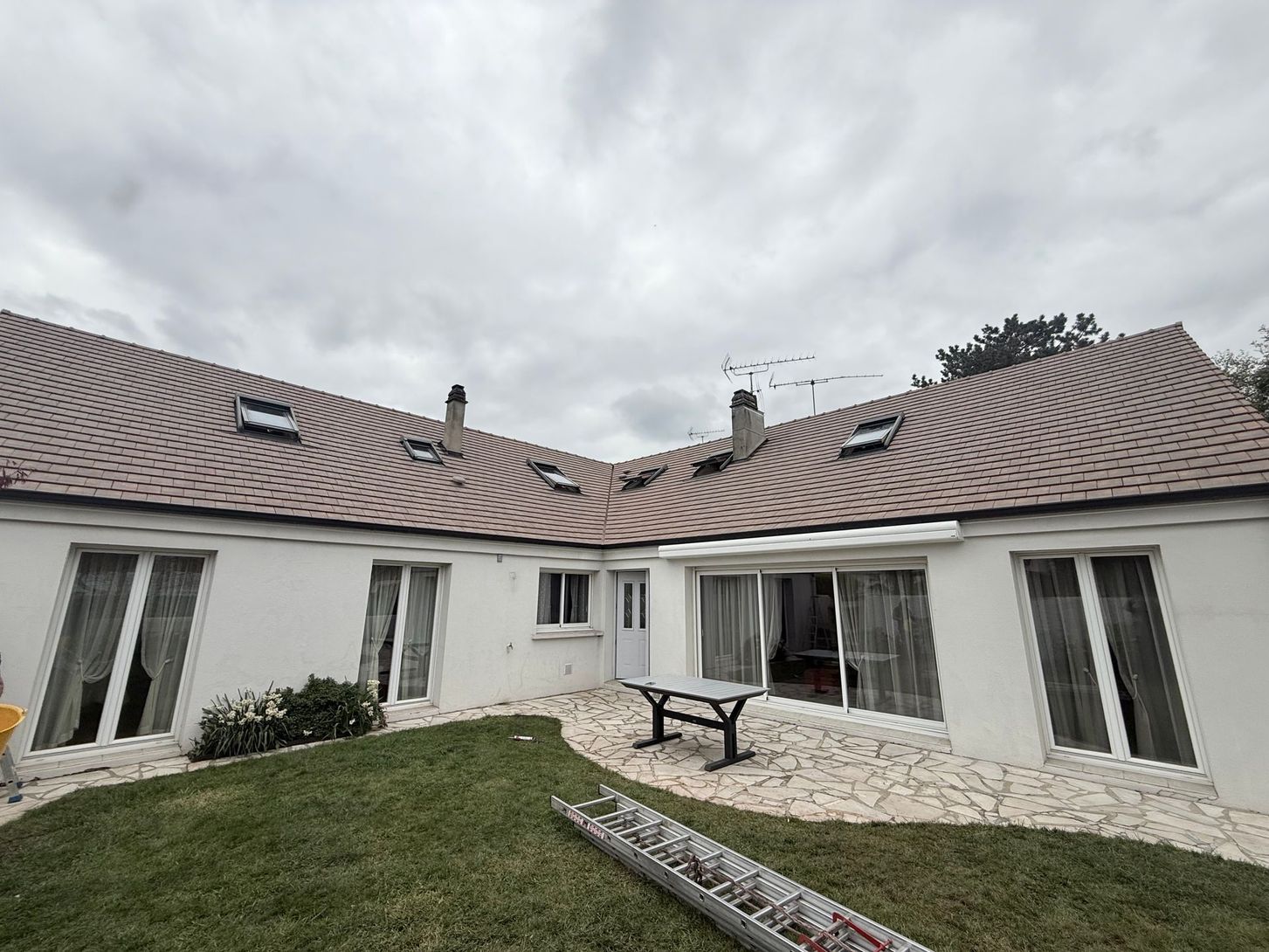 Cour intérieure avec maison blanche incurvée, toit brun ondulé, ciel nuageux, pelouse et table de pique-nique.