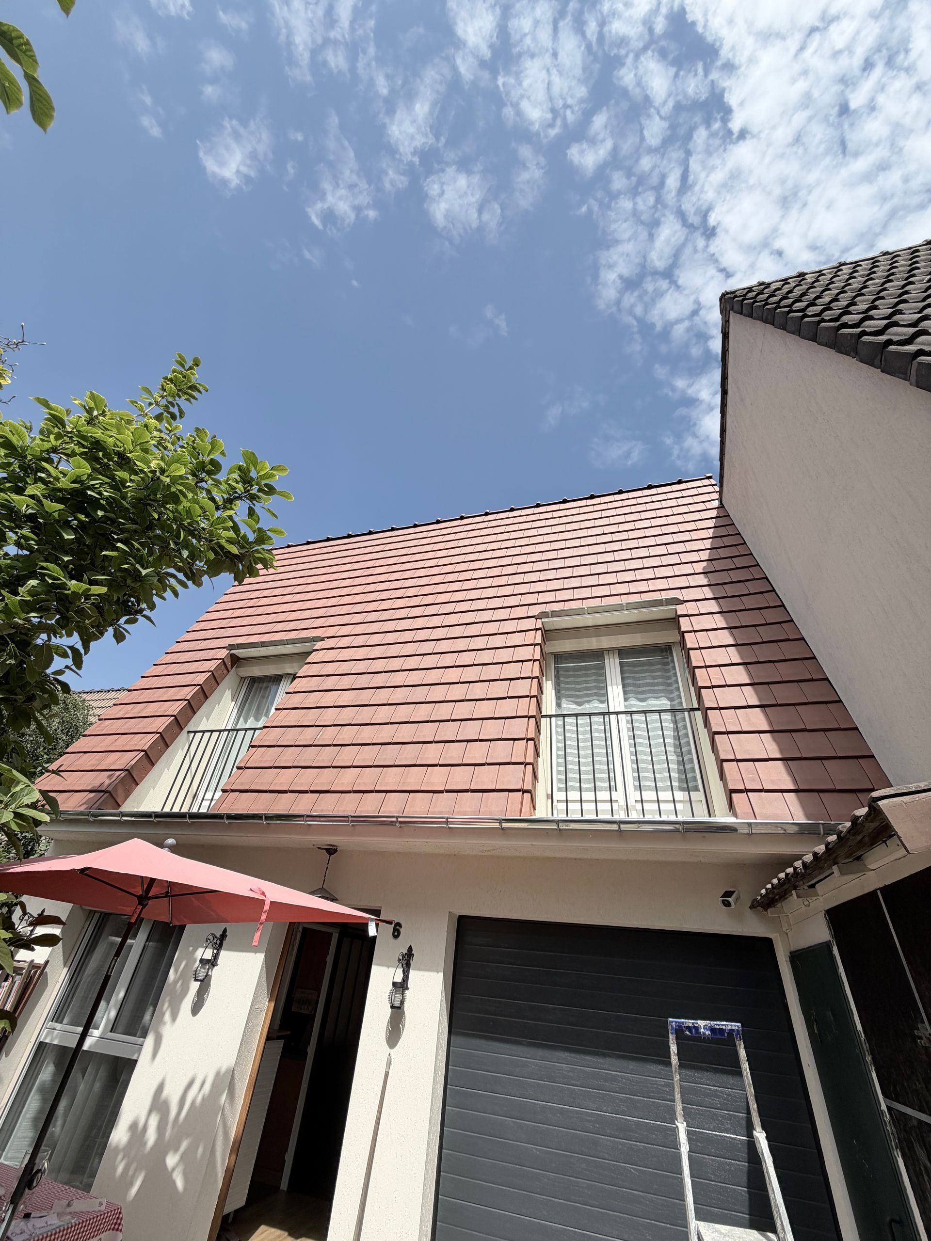 Vue en contre-plongée d'une maison au toit de tuiles rouges et aux murs blancs, sous un ciel bleu.