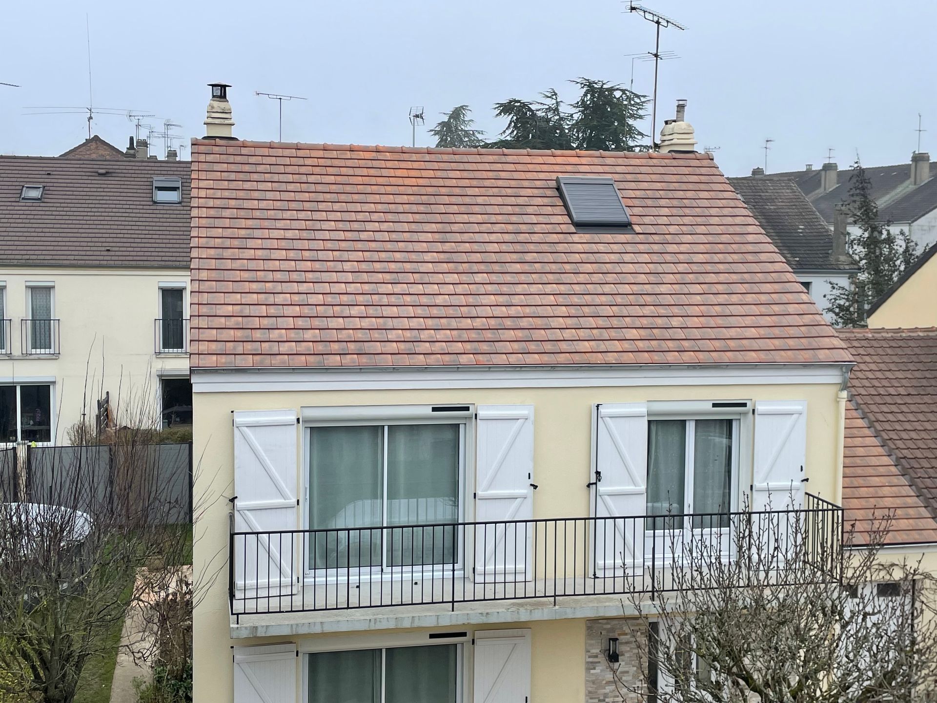 Petite maison aux volets blancs et au toit de tuiles rouges, vue de l'extérieur dans un quartier résidentiel.