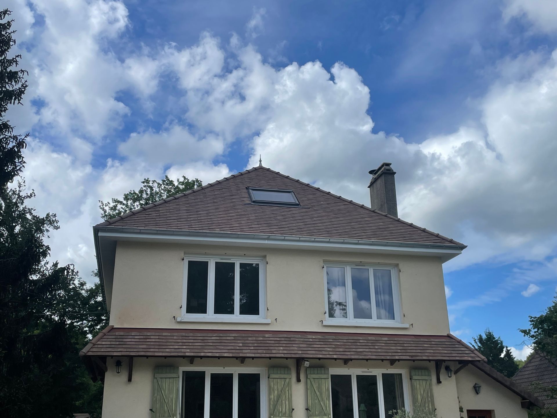 Maison à deux étages aux murs couleur crème et au toit de tuiles, sous un ciel bleu nuageux.