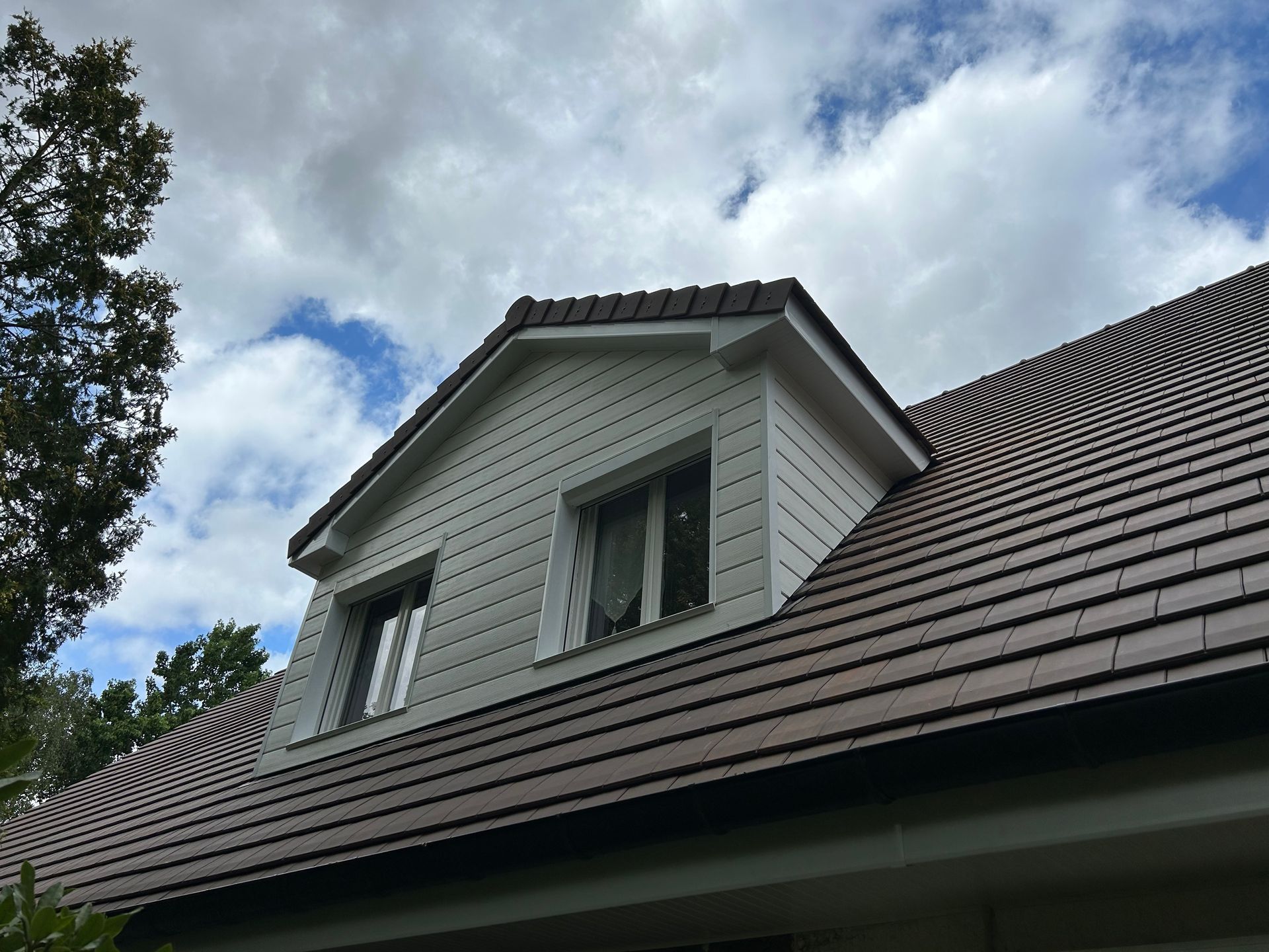 Toit de maison avec lucarnes blanches sous un ciel nuageux.