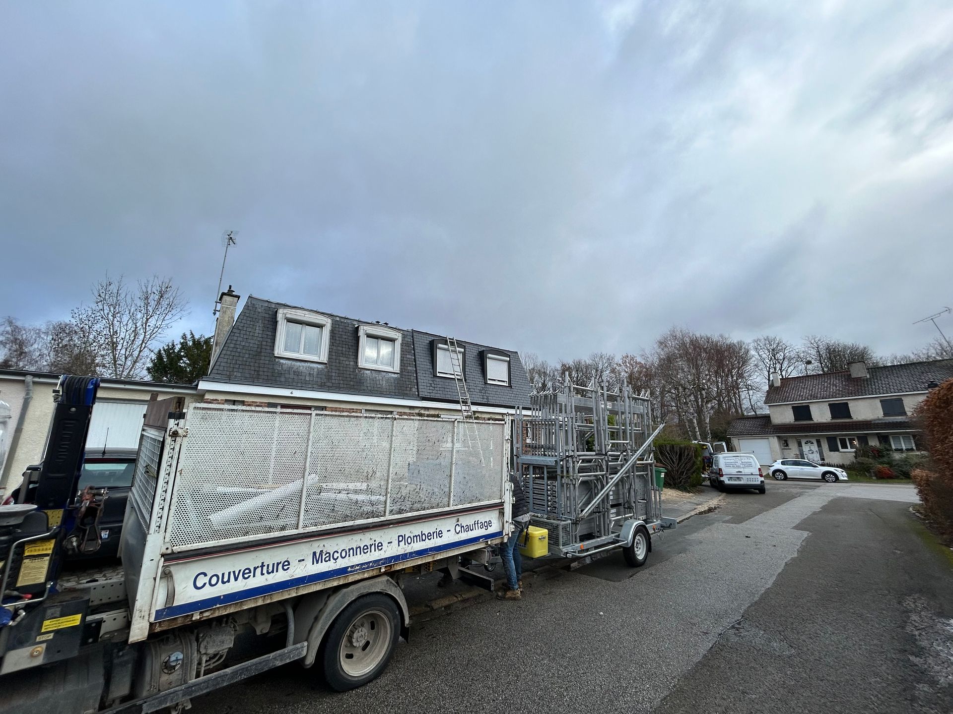 Camion de chantier dans une rue résidentielle sous un ciel nuageux, transportant une grosse cargaison emballée.