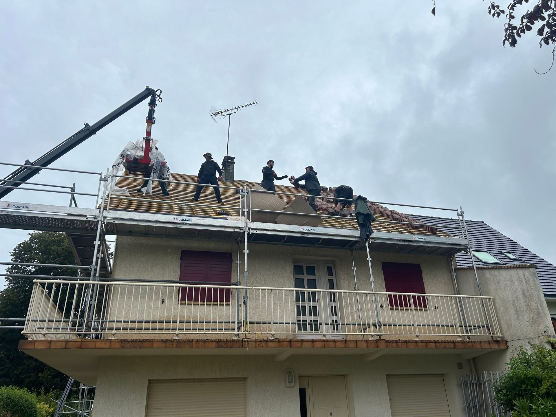 Des ouvriers réparent le toit d'une maison à l'aide d'échafaudages sous un ciel nuageux.