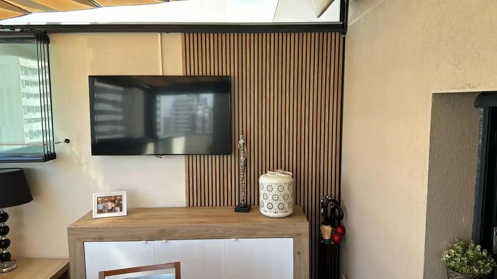 Televisor montado en una pared revestida de madera encima de un mueble en un acogedor espacio exterior.