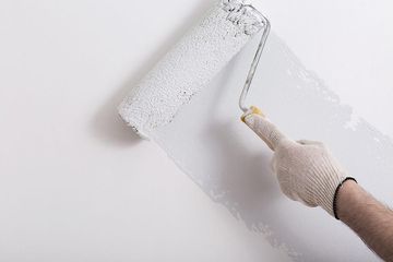 Una mano enguantada pinta una pared blanca con un rodillo de pintura.