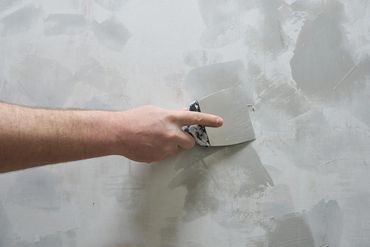 Una mano aplicando yeso gris a una pared con una llana.